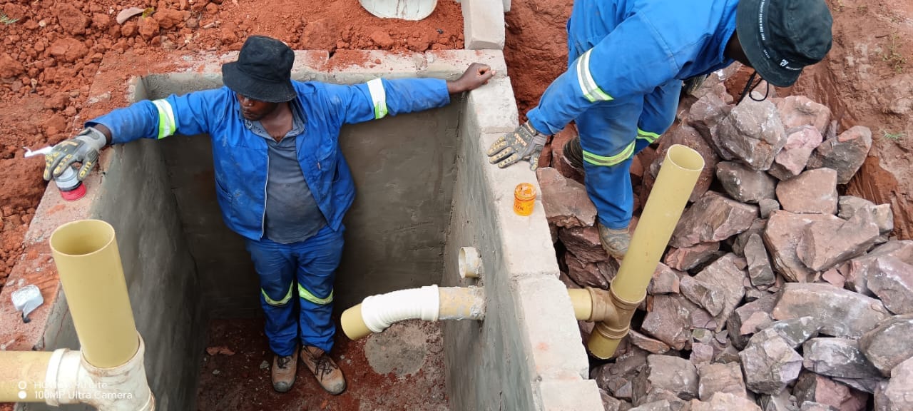 Plumbers fitting pipework inside a concrete drainage manhole
