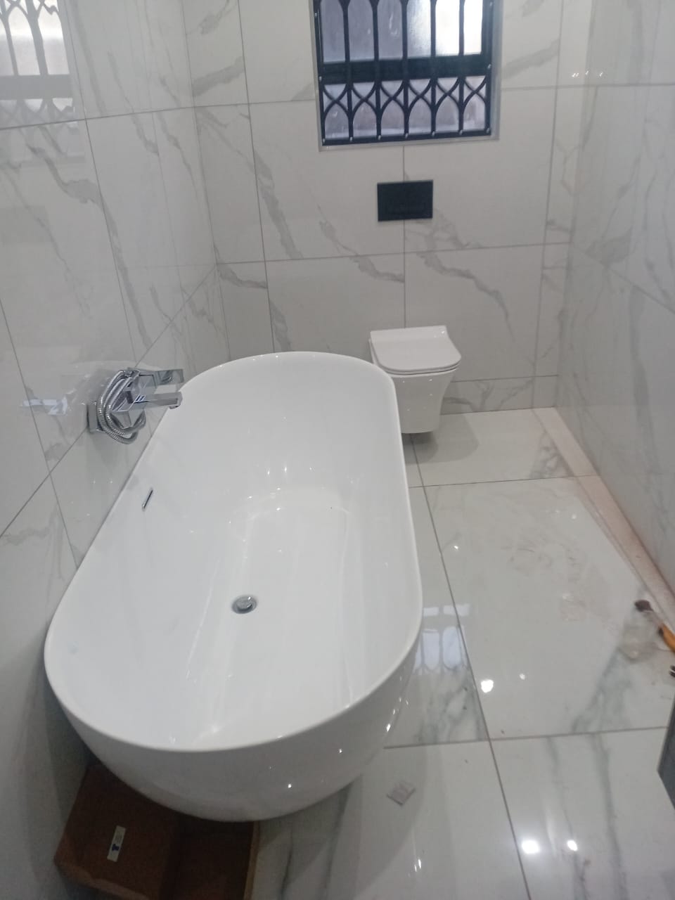 Freestanding bathtub with wall-mounted mixer and wall-hung toilet in a marble-tiled bathroom