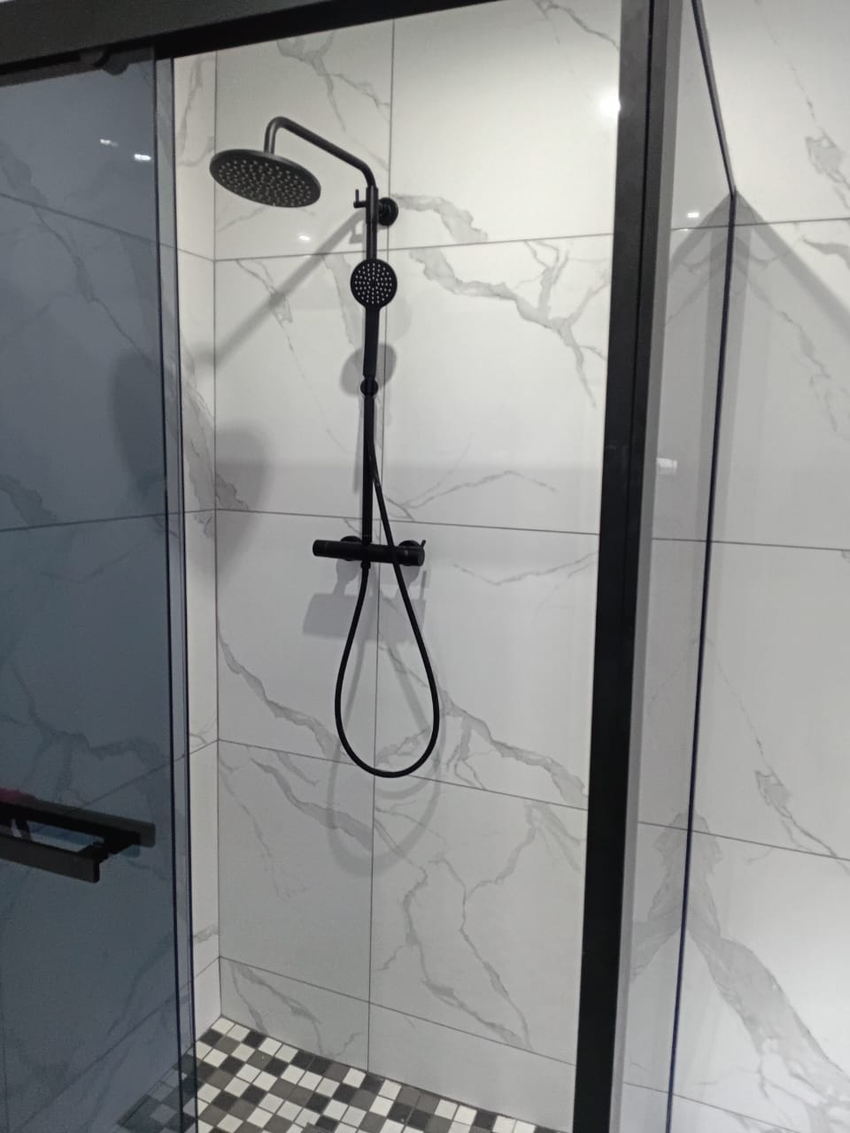 Black rain shower head and handheld shower fitted in a glass-enclosed shower